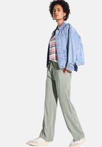 Džínová bunda, pruhované tričko a volné kalhoty světle zelené barvy. Bílé tenisky s texturovanými detaily. Neformální, pohodlný outfit.