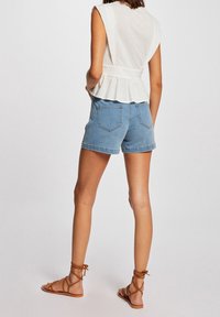 Top sin mangas de color beige claro con cintura peplum, combinado con pantalones cortos de mezclilla. Sandalias marrones de tiras completan el conjunto.