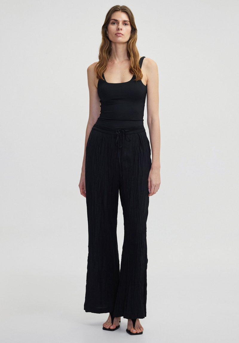 Zwarte mouwloze top en zwart gestreepte wijde pantalon met een koord in de taille. De stof lijkt licht en vloeiend.