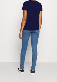 Mörkblå kortärmad t-shirt kombinerad med ljusblå tighta jeans och svarta slip-on skor. Enkelt utformad, utan synliga mönster eller grafik.