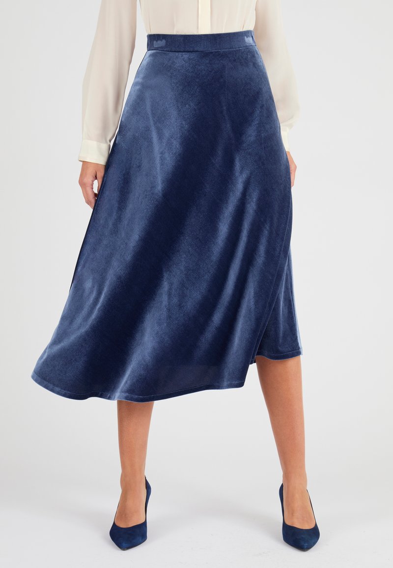 Falda de terciopelo azul marino hasta el tobillo con una silueta en A, que presenta una textura suave y una discreta abertura lateral. Combinada con tacones a juego.