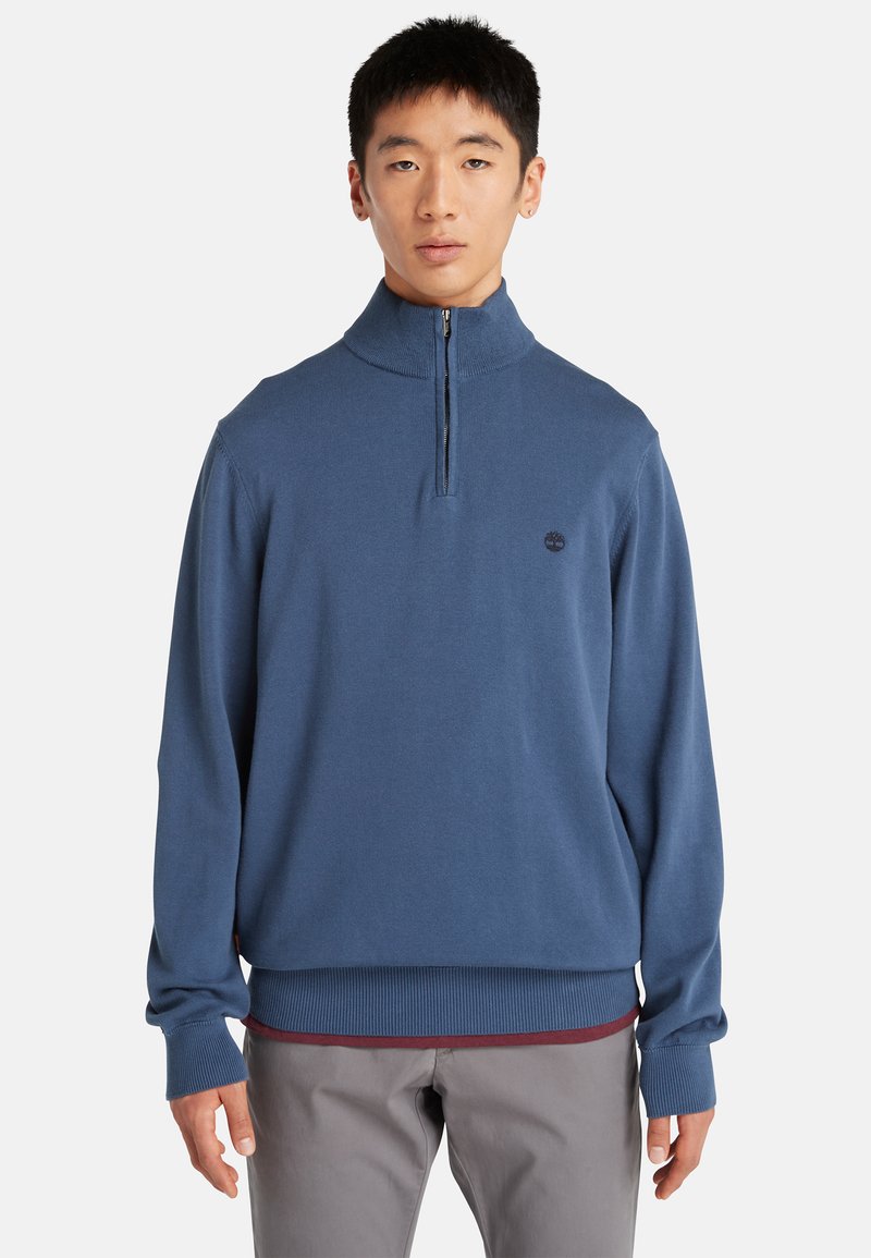 Pullover da uomo con zip e collo alto di colore blu scuro, realizzato in un tessuto morbido. Presenta polsini e orlo a coste, con un piccolo logo sul petto.