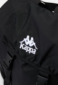 Zwarte nylon rugzak met een textuur oppervlak, een opvallend wit geborduurd Kappa-logo en verstelbare banden met een plastic gespsluiting.