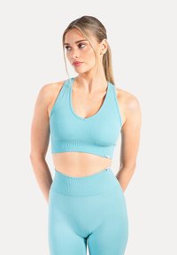 Sujetador deportivo azul claro con textura acanalada, escote redondo y tirantes anchos, combinado con leggings a juego de cintura alta que tienen un detalle recortado.