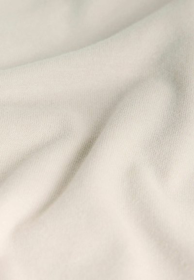 Nærbillede af blødt, cremefarvet stof med blide folder og synlig finstrikket tekstur.
