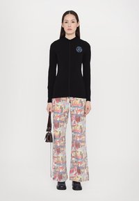 Top negro de manga larga con cuello alto y logo azul, combinado con pantalones acampanados con un estampado gráfico colorido. Lleva un bolso pequeño.