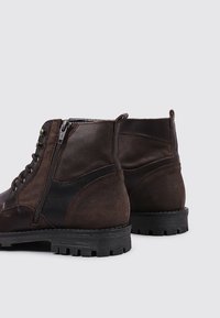 Bottines en cuir brun avec une finition texturée, fermeture éclair sur le côté, bout rond et une semelle en caoutchouc noir durable avec des crans profonds.