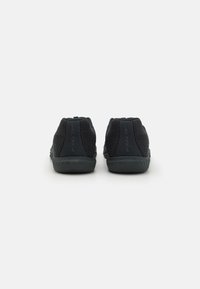 Chaussures de sport noires avec un dessus en maille, un design élégant, un talon courbé et une semelle extérieure en caoutchouc texturé pour une adhérence et une flexibilité.