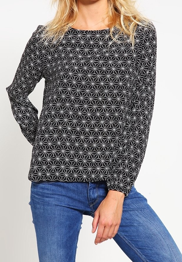 Svart långärmad blus med ett vitt stjärnblossmönster, rund halsringning och elastiska ärmslut, i kombination med blå jeans.