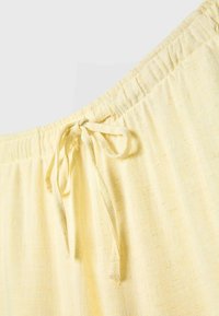 Pantalon en tissu jaune clair avec une taille élastique et un cordon noué à l'avant.