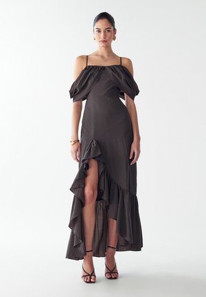 Tmavohnedé šaty s odhalenými ramenami a volánkovým lemom, ktoré majú rozparok až po stehná a sú vyrobené z mäkkej textúrovanej tkaniny. Vyzerajú skvelo spolu s čiernymi sandálmi na remienky.