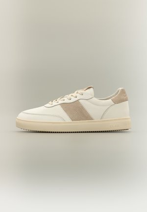 Nízký béžový teniska s předním zavazováním na tkaničky, perforovaným semišovým bočním panelem a gumovou podrážkou na neutrálním pozadí.