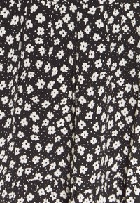 Tissu noir avec un motif de petites fleurs blanches et de points blancs, légèrement texturé avec des plis visibles.