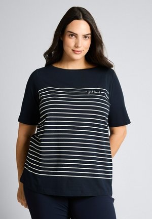 Frau mit langen dunklen Haaren, die ein marineblaues T-Shirt mit weißen horizontalen Streifen und dem Schriftzug "good times" auf der Brust trägt.