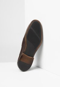 Scarpa in pelle marrone con superficie texturizzata, punta arrotondata e suola in gomma piatta. La suola presenta una trama per garantire aderenza.