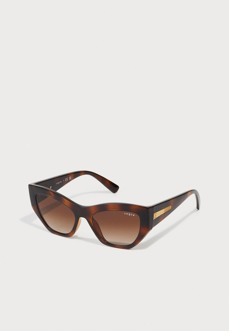 Óculos de sol estilo gato com uma armação de tartaruga brilhante, lentes castanhas em degradê e detalhes em dourado nas hastes.