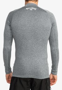 Camisa de baño de manga larga gris con tejido texturizado, diseño ajustado y costuras en contraste. El logo "Billabong" está exhibido en el cuello.