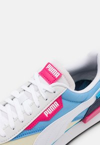 Baskets PUMA présentant un mélange de matériaux texturés en blanc, bleu clair et rose, avec un marquage visible et des accents contrastants.