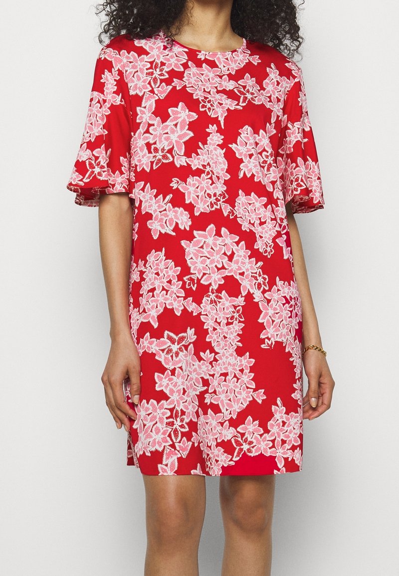 Robe rouge avec un motif floral en rose clair. Manches courtes avec une coupe décontractée. Tissu lisse avec un col rond.