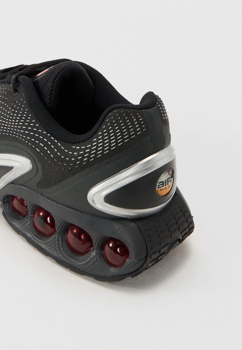 Czarne sneakersy z teksturowaną siateczkową cholewką, srebrnymi akcentami i charakterystyczną podeszwą z poduszką powietrzną, na której znajdują się czerwone bąble i wzorzysta powierzchnia.