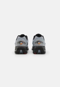 Vista trasera de zapatillas de running con una parte superior de malla gris, acentos negros y una suela negra texturizada con detalles rojos y amortiguación Air visible.