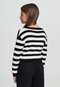 Maglione a righe bianche e nere in maglia con vestibilità rilassata, texture a costine e scollatura ampia, abbinato a jeans neri.