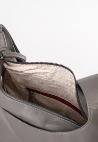 Graue Lederhandtasche, geöffnet, um das leicht gemusterte Innenfutter mit einer kleinen Reißverschlusstasche zu zeigen.