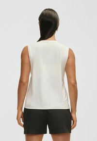 Bezramionowy biały top sportowy o gładkiej fakturze, okrągłym dekolcie i luźnym kroju, w komplecie z czarnymi szortami.