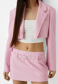 Blazer corto rosa e gonna coordinata con cintura. Texture liscia, design sartoriale, dettaglio con tasca frontale sul blazer e accenti in metallo argentato.
