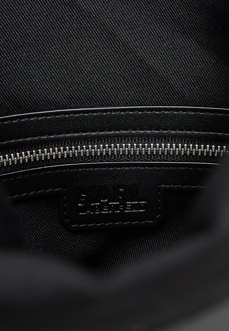 Intérieur d'un sac en tissu noir avec une accent en cuir lisse et une fermeture éclair argentée. Logo embossé "KARL LAGERFELD" visible sur le patch en cuir.