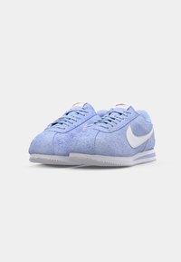 Zili zili sporta apavi, kas izgatavoti no zila zamšāda ar baltu swoosh logotipu un tekstūrētām akcentiem, ar gumijas zoli un kontrastējošiem baltajiem elementiem.