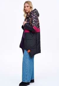 Pohodlná bunda s květinovou kapucí a černým tělem s růžovým akcentem. Obsahuje zip a oranžovou nášivku s logem. Nosená přes široké džíny.