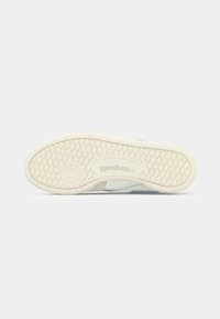 Potplat bijele Reebok tenisice s dijamantskim i kružnim uzorkom na svijetlosivoj pozadini.