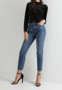 Sort velour langærmet top med blomstermønster, parret med højalstede lyseblå jeans og sorte strophæle.