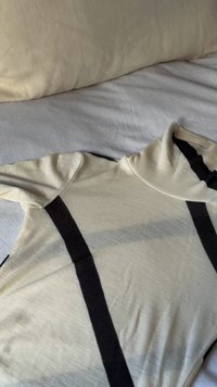 Krémově zbarvený rolákový svetr s černými vertikálními pruhy položený na světle šedém žebrovaném textilním povrchu.