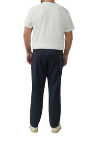 Herenoutfit met een witte shirt met korte mouwen en marineblauwe broeken met een achterzak. De schoenen zijn crèmekleurig met een gestructureerde zool.