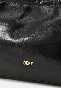Musta nahkalaukku, jossa on sileä ja kiiltävä pinta. Etupuolella on kultainen DKNY-logo. Yksinkertainen muotoilu, ilman lisävarusteita tai kuvioita.