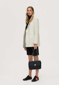 Black quilted handbag with silver chain strap, paired with a cream blazer, black turtleneck, and black shorts, featuring black and orange sneakers.