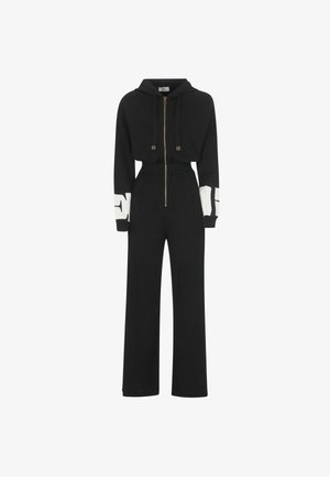 Tuta nera realizzata in tessuto morbido, con zip frontale, cappuccio e gambe larghe. Presenta dettagli bianchi sulle maniche e accessori in oro.