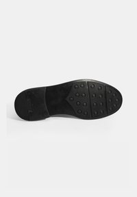 Semelle de chaussure en caoutchouc noir présentant une surface texturée avec des motifs circulaires et un design fendu près du talon pour une meilleure adhérence.