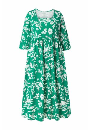 Vihreä kukkakuosinen mekko, jossa on kolme neljänneksen hihaa, vartalonmyötäinen yläosa ja laskeutuva, kerroksittain laskeutuva hame, joka on koristeltu valkoisilla kukka- ja lehtikuoseilla.