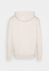 Felpa color crema con cappuccio curvo, polsini e orlo a coste. Tessuto morbido e liscio senza motivi o loghi visibili sul retro.