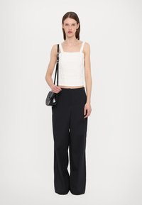 White cropped top with textured detailing, paired with high-waisted black wide-leg trousers. Model holds a small black handbag.