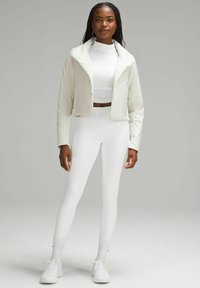 Biała krótka kurtka o miękkiej teksturze, zestawiona z dopasowanymi białymi legginsami. Strój obejmuje bluzkę z wysokim kołnierzem oraz białe trampki.