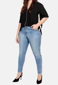 Haut noir à manches courtes avec un motif blanc, associé à un jean skinny bleu clair. Modèle portant des chaussures à talons hauts noires.