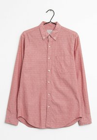 Chemise rouge à boutons avec un tissu texturé, petits motifs blancs, col, manches longues, et une poche poitrine. Accrochée à un crochet noir.