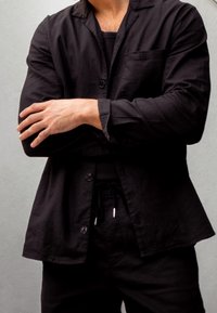 Czarna lniana kurtka z kołnierzem, z pojedynczą kieszenią, zapięciem na guziki oraz luźnym krojem, w połączeniu z pasującymi spodniami na sznurek.