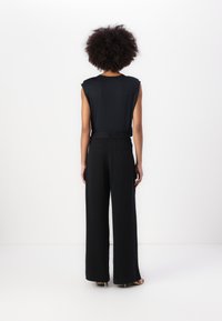 Black sleeveless top with subtle shoulder detailing paired with black wide-leg trousers. Smooth fabric with a loose fit and clean lines.