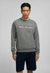 Grijze sweatshirt met ribgebreide manchetten, met het woord "HECHTER" in vetgedrukte, kleurrijke letters, gecombineerd met marineblauwe shorts. Gladde stofstructuur.
