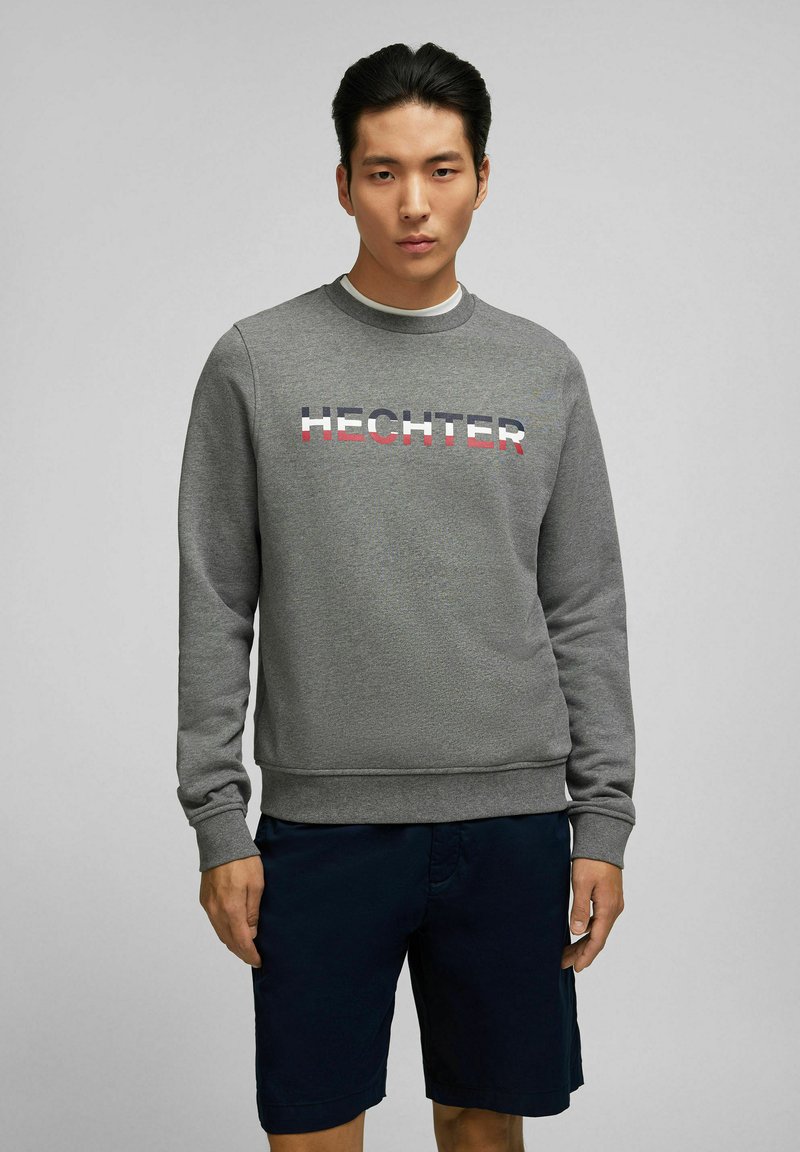 Grijze sweatshirt met ribgebreide manchetten, met het woord "HECHTER" in vetgedrukte, kleurrijke letters, gecombineerd met marineblauwe shorts. Gladde stofstructuur.